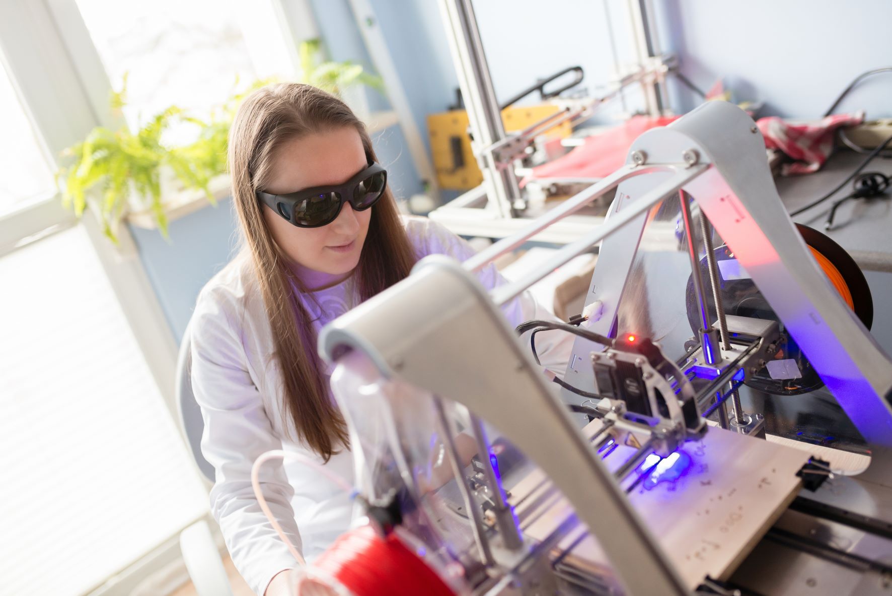 Woman in white lab coat and protective glasses working with laser engraver